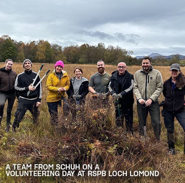 Image of a Schuh team outdoors at RSPB Loch Lomond, holding tools during a conservation volunteering day.