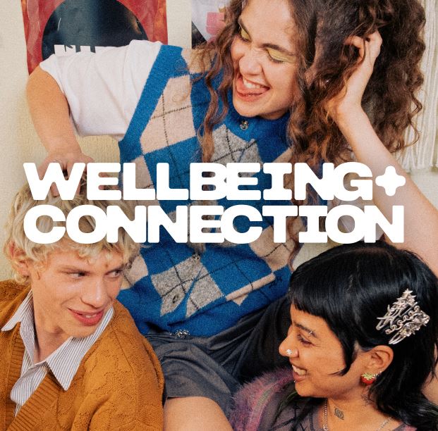 Text reads “Wellbeing + Connection” over a cozy indoor setting with group of friends.