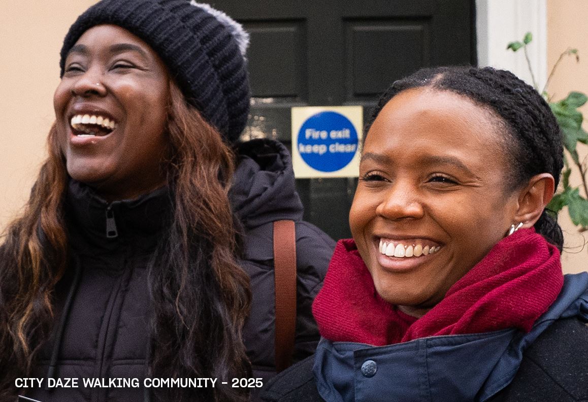 Image of two smiling people in winter clothes outside a building, with “City Daze Walking Community – 2025